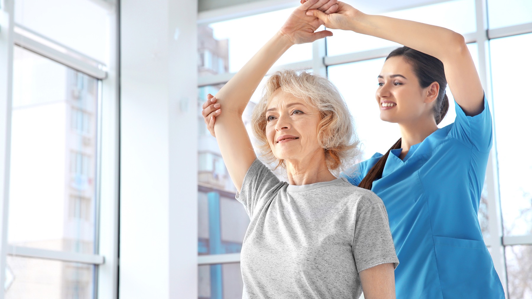Physiotherapist helping an older woman stretch her arms